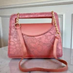 Brick red embossed floral mini crossbody bag displayed with long gold chain and shoulder pad for comfortable wearing