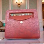 Brick red embossed floral mini crossbody bag with flap open showing magnetic closure inner space and floral texture