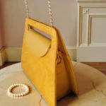 Side angle of embossed floral mustard yellow mini crossbody bag displayed on table