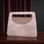 Soft pink embossed floral mini carry crossbody handbag front view on wooden table with velvet curtain background