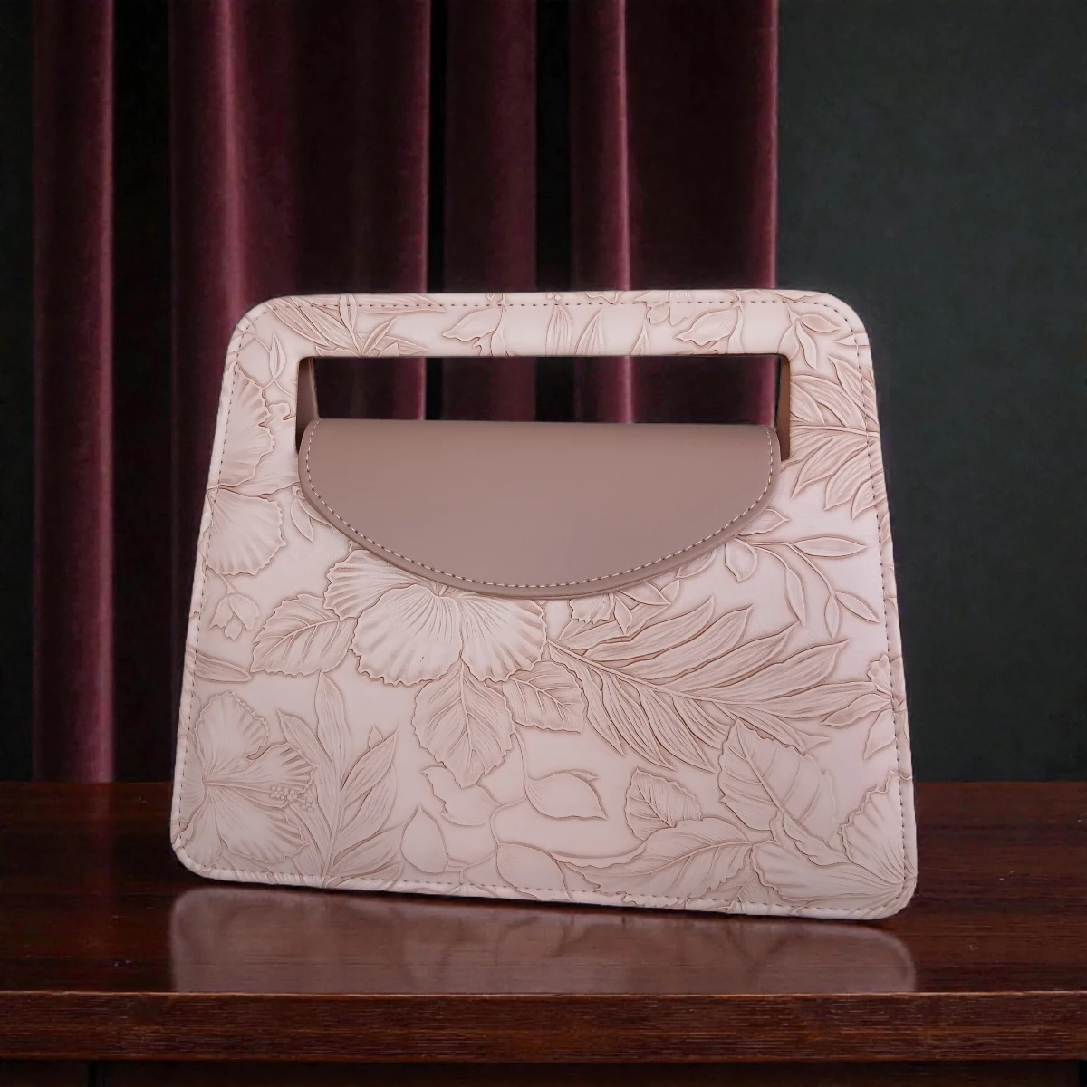 Soft pink embossed floral mini carry crossbody handbag front view on wooden table with velvet curtain background