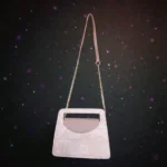 Soft pink embossed floral mini carry crossbody handbag hanging with long chain strap against starry black backgroun