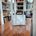 Embossed koi leather shoulder handbag in ice blue, front view on wooden table