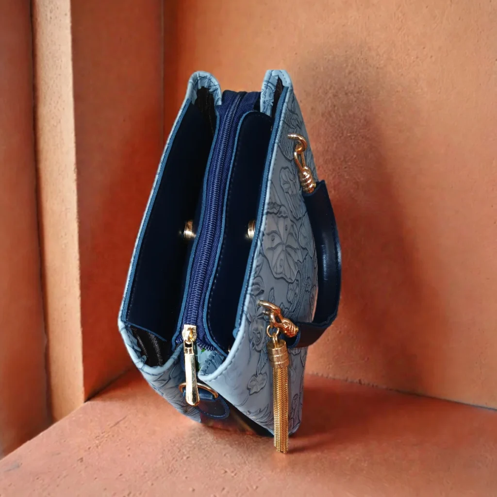 Embossed koi leather shoulder handbag in ice blue, side angle view on concrete surface