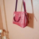 Hanging view of embossed maroon koi leather shoulder handbag against wall