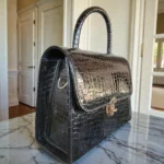 Side view of glossy black croc structured handbag showing depth, stitching, and metal hardwar