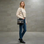 Model holding glossy black croc top handle handbag in front of mirror in an indoor setting