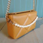 Side angle of camel quilted crossbody handbag showing gold chain strap