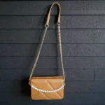 Camel quilted crossbody handbag hanging with long chain strap against black wall