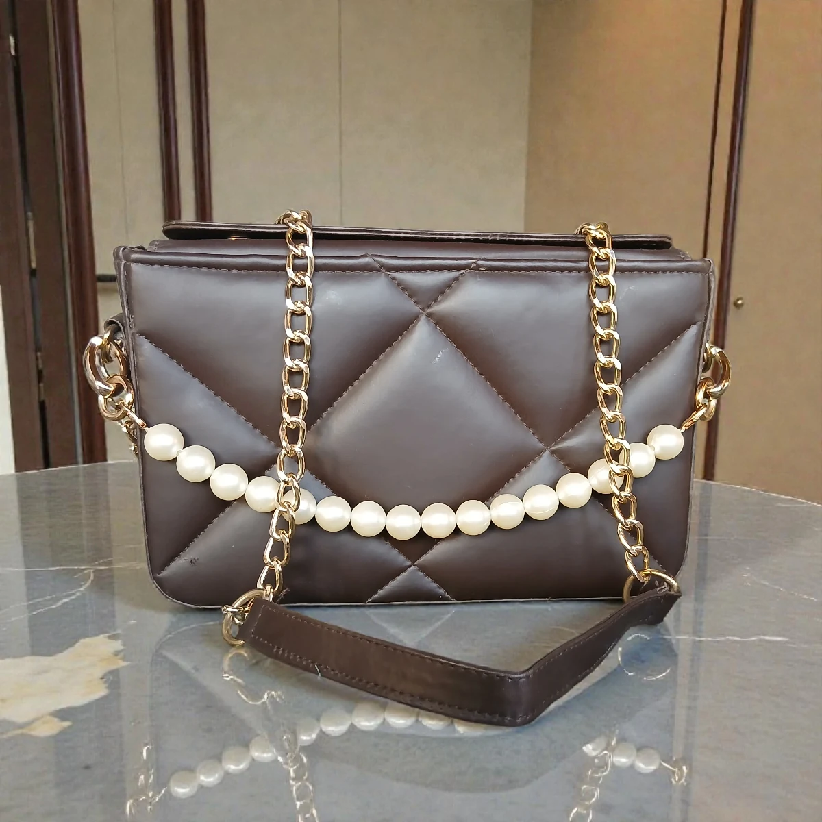 Coffee brown quilted crossbody bag with pearl chain and gold chain strap on table