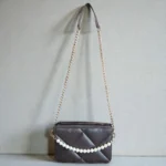 Coffee brown quilted crossbody bag with pearl chain and gold strap hanging on wall
