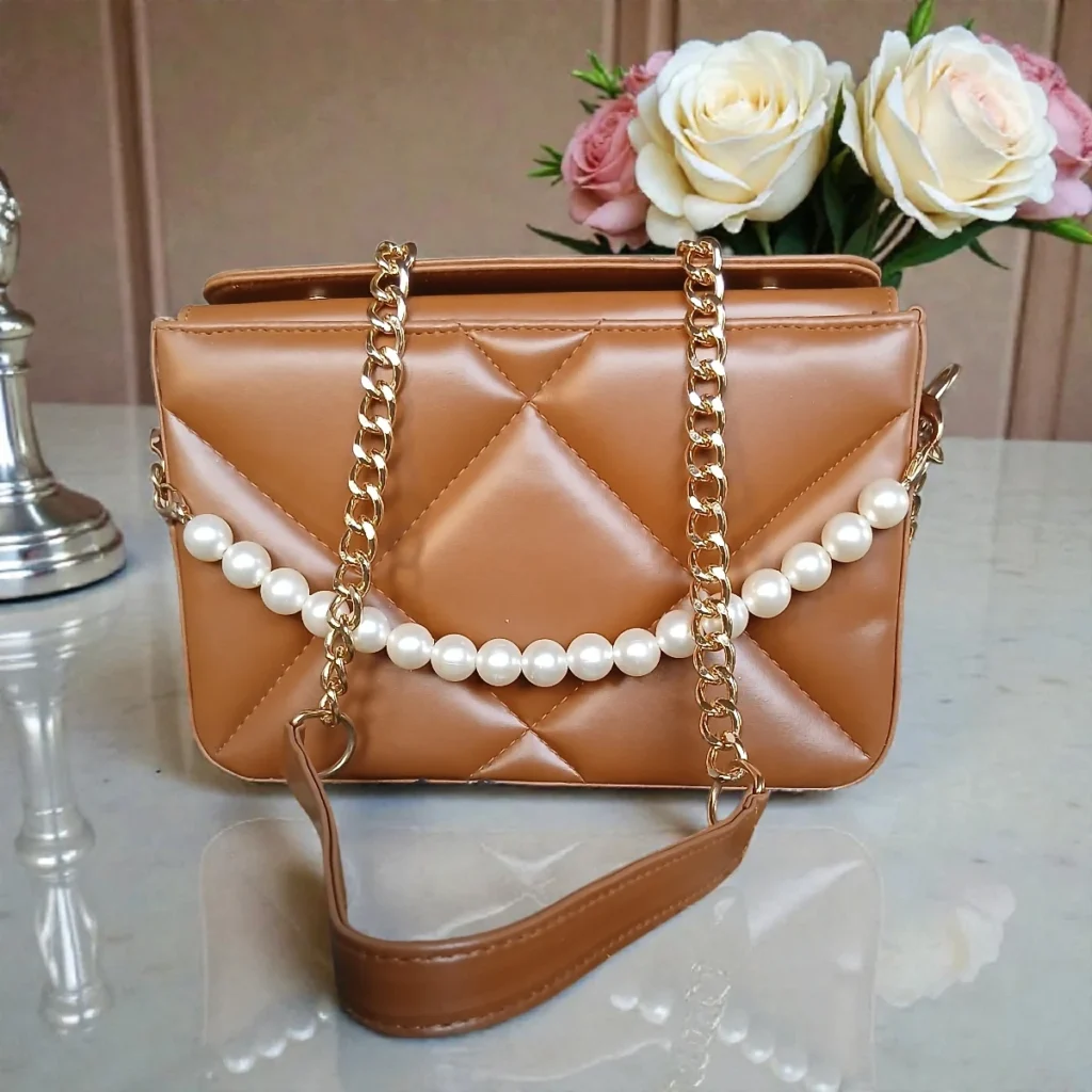 Tan brown pearl chain quilted crossbody bag on table with gold chain strap