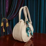 Beige drawstring pouch handbag side view showing scarf and hanging charm