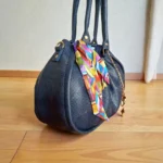 Side view of navy blue soft drawstring handbag with gold hardware