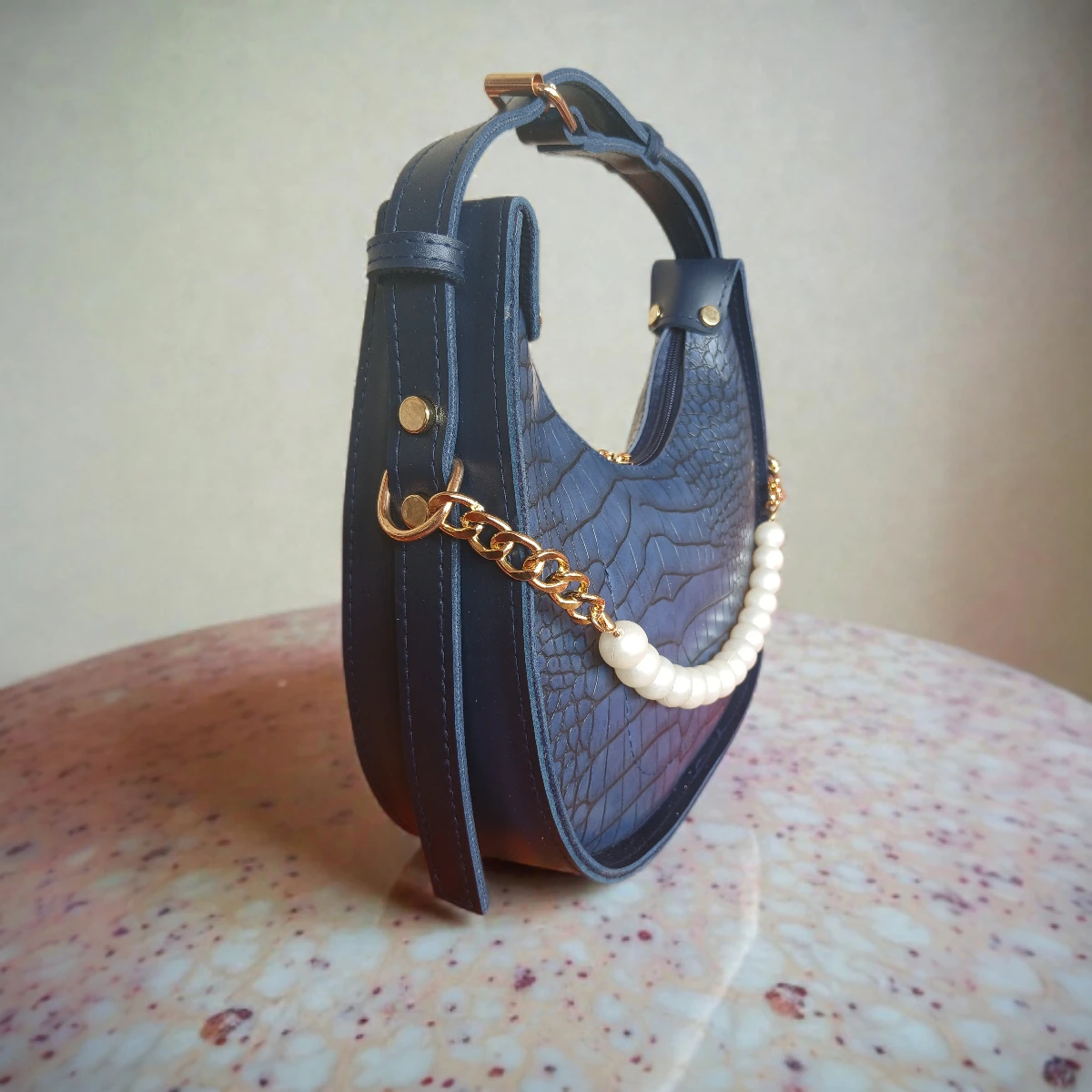 Side view of navy blue crossbody bag with pearl detail