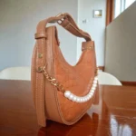 Tan brown pearl detail crossbody bag styled indoors on table with elegant background