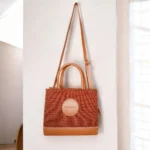 Brown tweed crossbody handbag hanging by its long adjustable strap on a wall