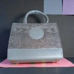 Detailed front view of grey tweed crossbody handbag showing base and metal studs