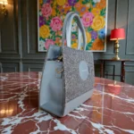 Side angled view of grey tweed crossbody handbag on a marble table with floral background