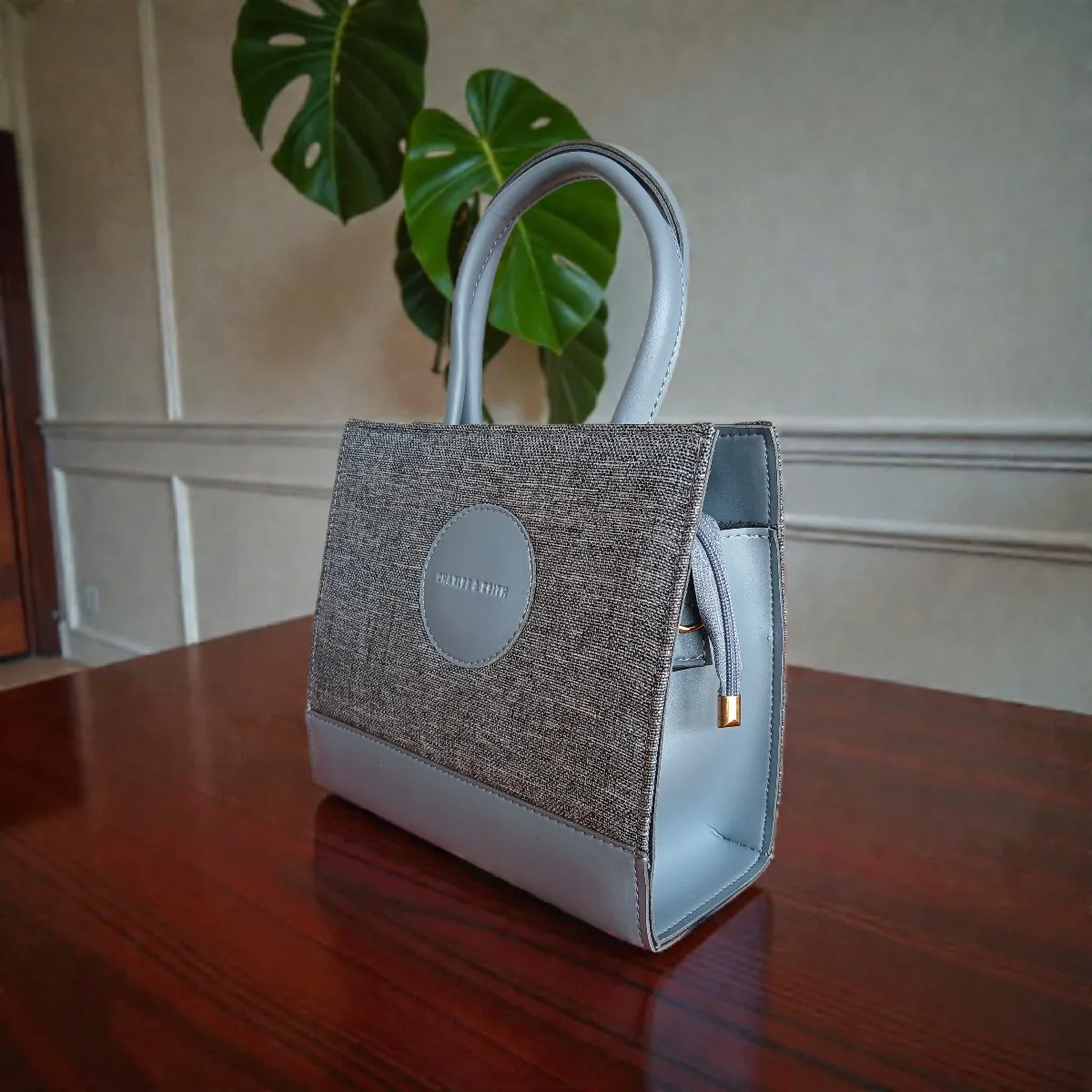 Side profile of grey tweed crossbody handbag showing textured design and leather handles