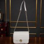 Embossed grid leather flap chain crossbody bag in ivory white with gold chain strap and twist lock closure displayed on wooden tab