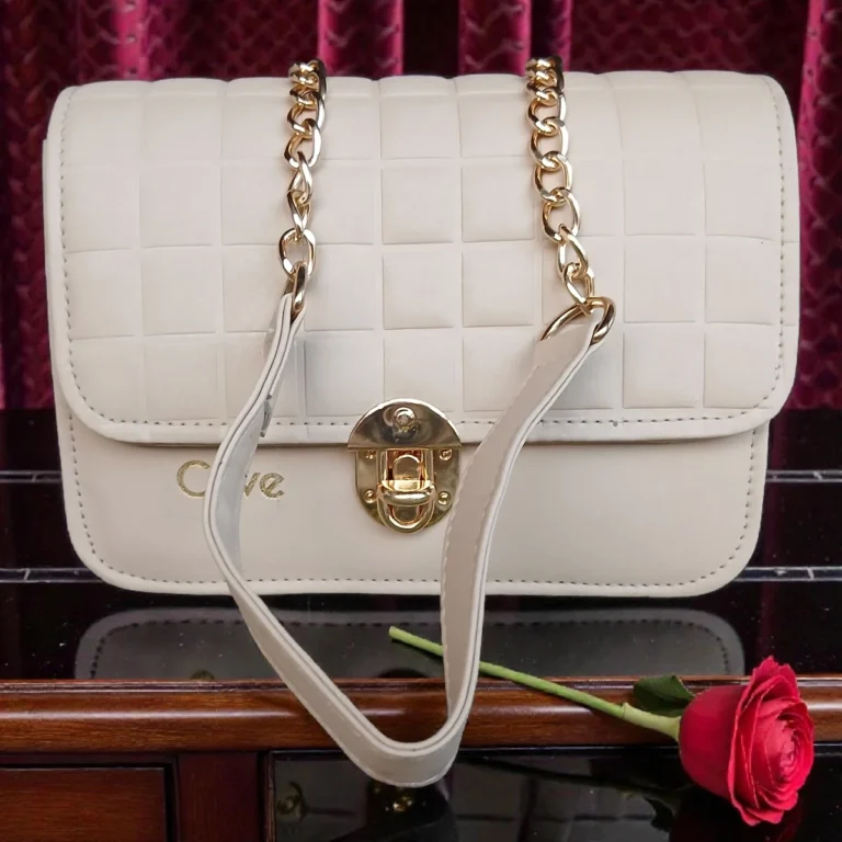 Front display of ivory white embossed grid leather flap crossbody bag with gold chain strap placed on wooden table with rose
