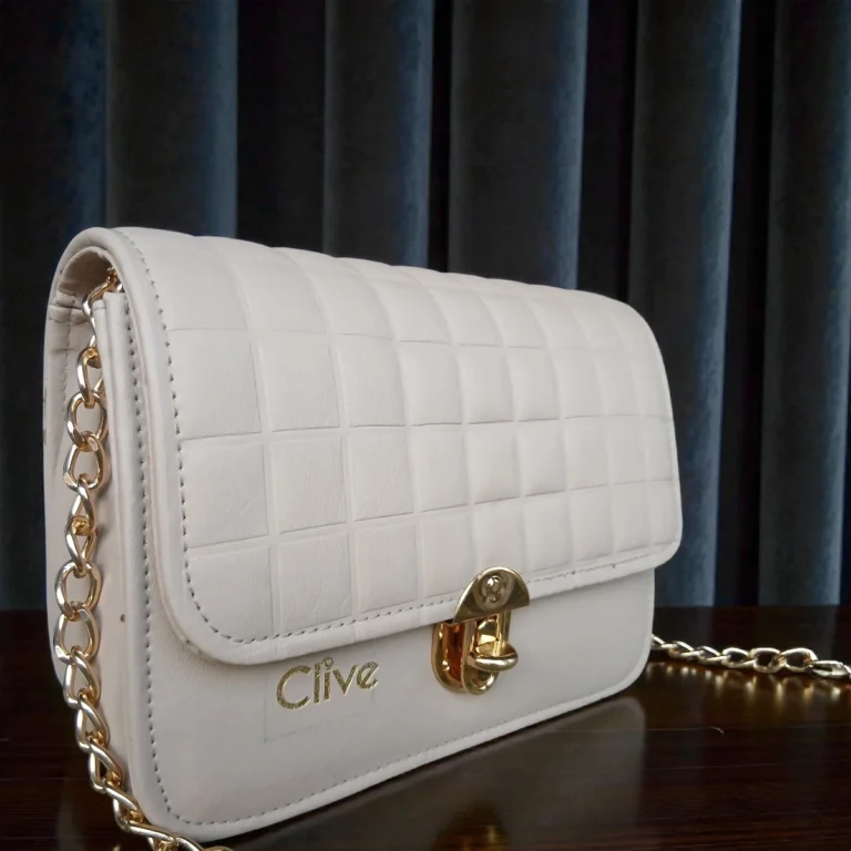 Angled side view of ivory white embossed grid leather flap crossbody bag with gold chain strap and structured body
