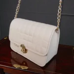 Angled side view of ivory white embossed grid leather flap crossbody bag with gold chain strap and structured body
