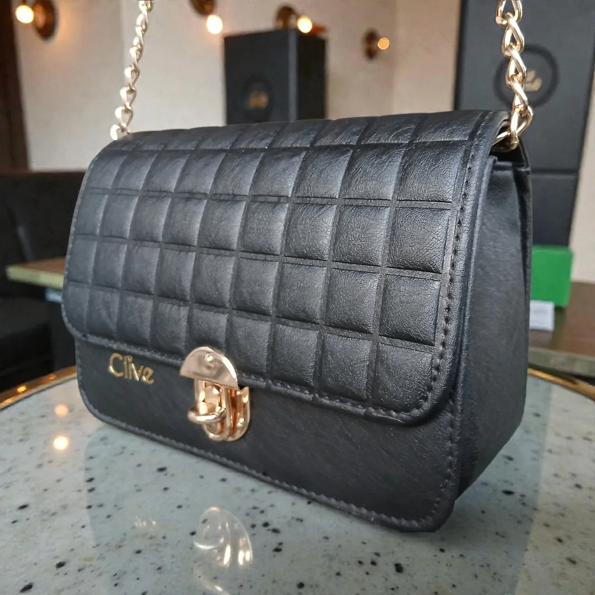 Close-up side angle of jet black embossed grid leather crossbody bag showing flap texture and gold turn-lock closure