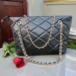 Front view of Classic Quilted Chain Strap Tote Bag – Jet Black with long gold chain handles styled on wooden surface with decorative flowers