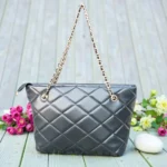 Classic Quilted Chain Strap Tote Bag – Jet Black placed outdoors near a wooden door featuring glossy quilted texture and gold tone chain hardware
